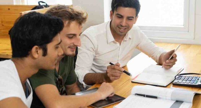 Hands arranging sentence cards for PTE Reading Reorder Paragraphs preparation, with study notes and a laptop on a desk.